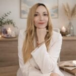 Portrait de Céline Baron assise à son bureau, vêtue d'un blazer blanc, dans un environnement serein avec des bougies et des cristaux