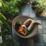 Vue aérienne d'une femme se relaxant avec un café dans un fauteuil en rotin, au cœur d'un aménagement d'un jardin bien-être verdoyant