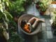 Vue aérienne d'une femme se relaxant avec un café dans un fauteuil en rotin, au cœur d'un aménagement d'un jardin bien-être verdoyant