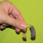 Une main tient un appareil auditif avec embout sur fond vert