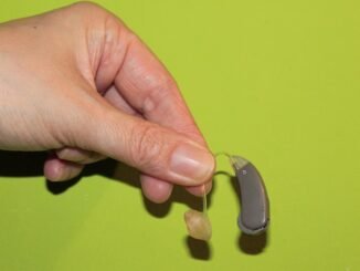 Une main tient un appareil auditif avec embout sur fond vert