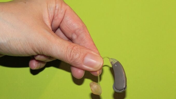 Une main tient un appareil auditif avec embout sur fond vert